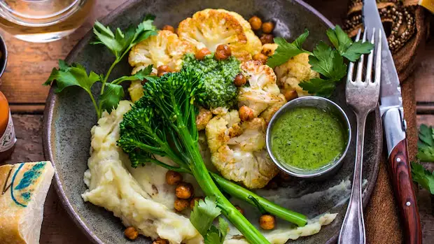 Golden-brown roasted cauliflower steaks drizzled with homemade chimichurri