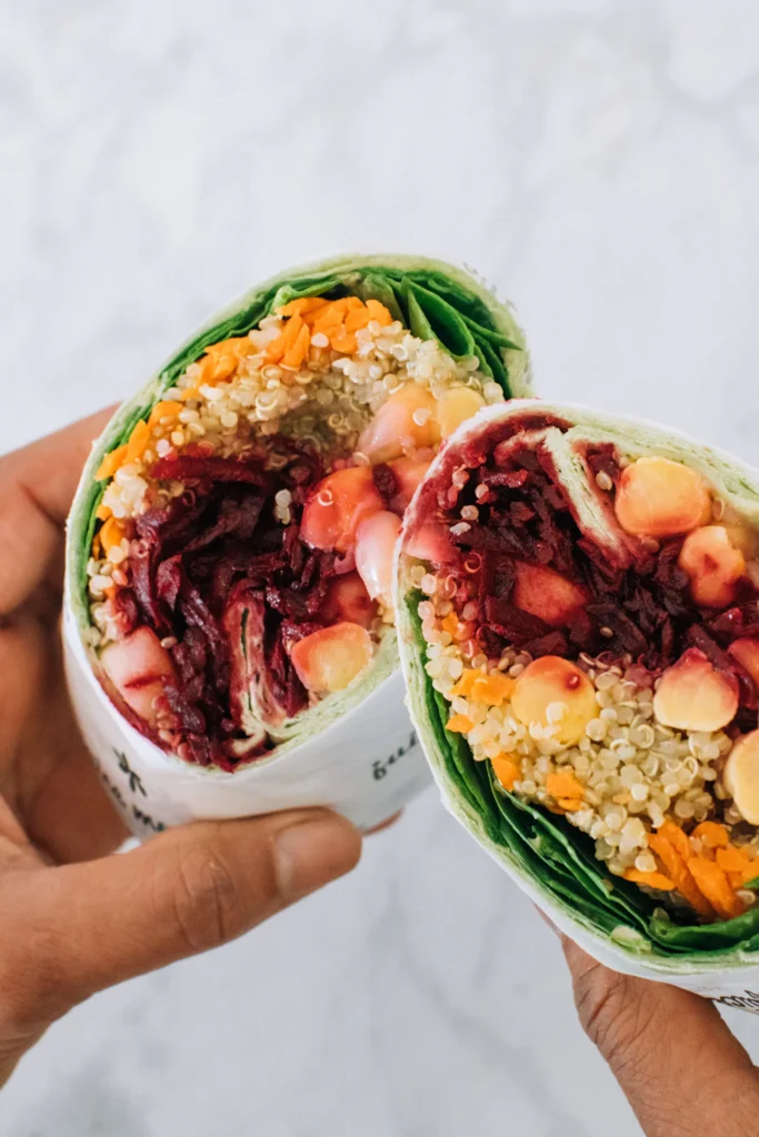 Hands holding a halved avocado buffalo chickpea salad wrap