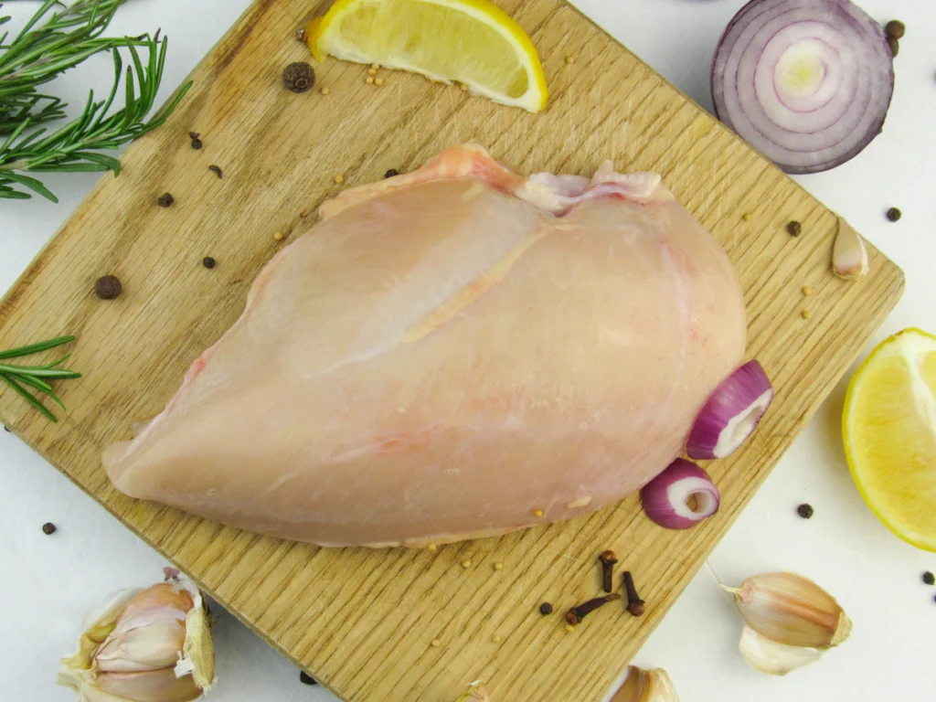 Raw chicken breast with garlic and lemon on a cutting board, ready for a cottage cheese chicken bake