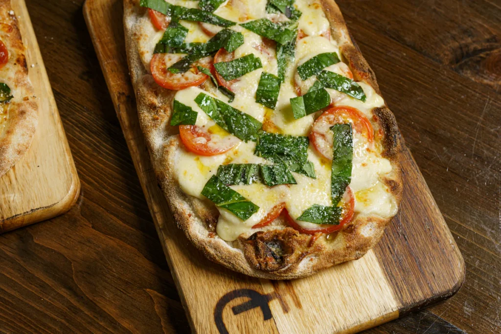 Flatbread pizza topped with tomato, melted cheese, and fresh basil on a board