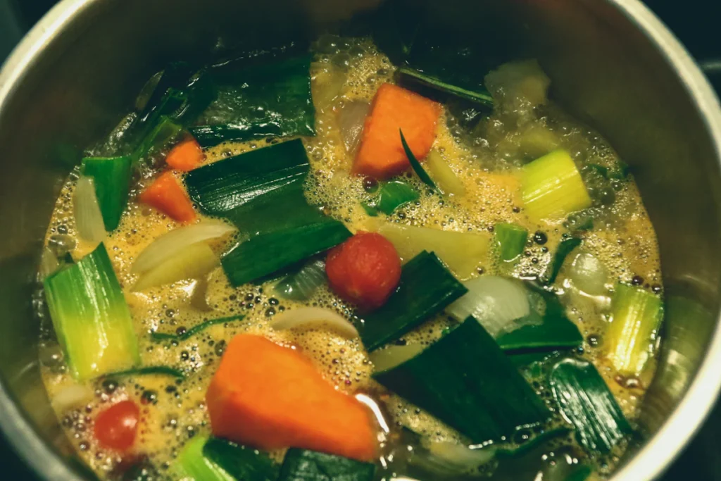 Pot of vegetable cabbage soup simmering with carrots and greens