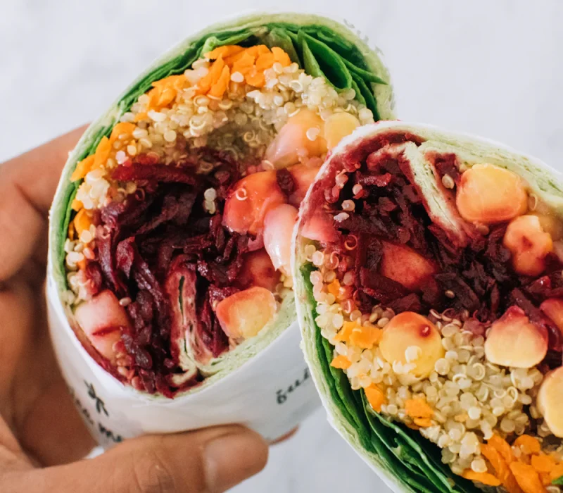 Hands holding a halved avocado buffalo chickpea salad wrap